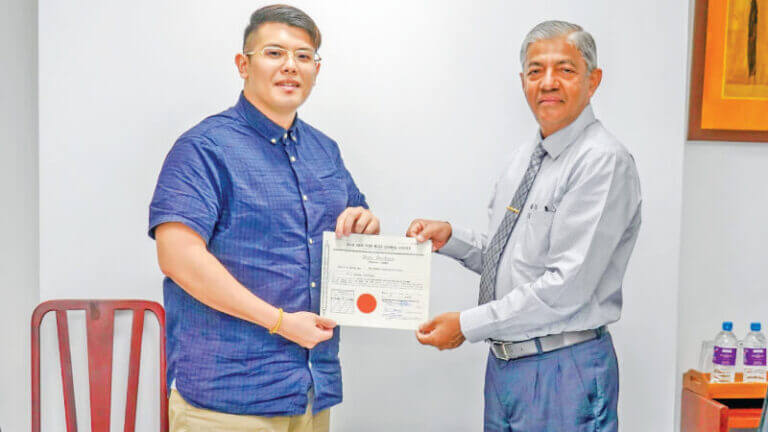 Two men proudly displaying a certificate in front of a desk, symbolizing their achievement.